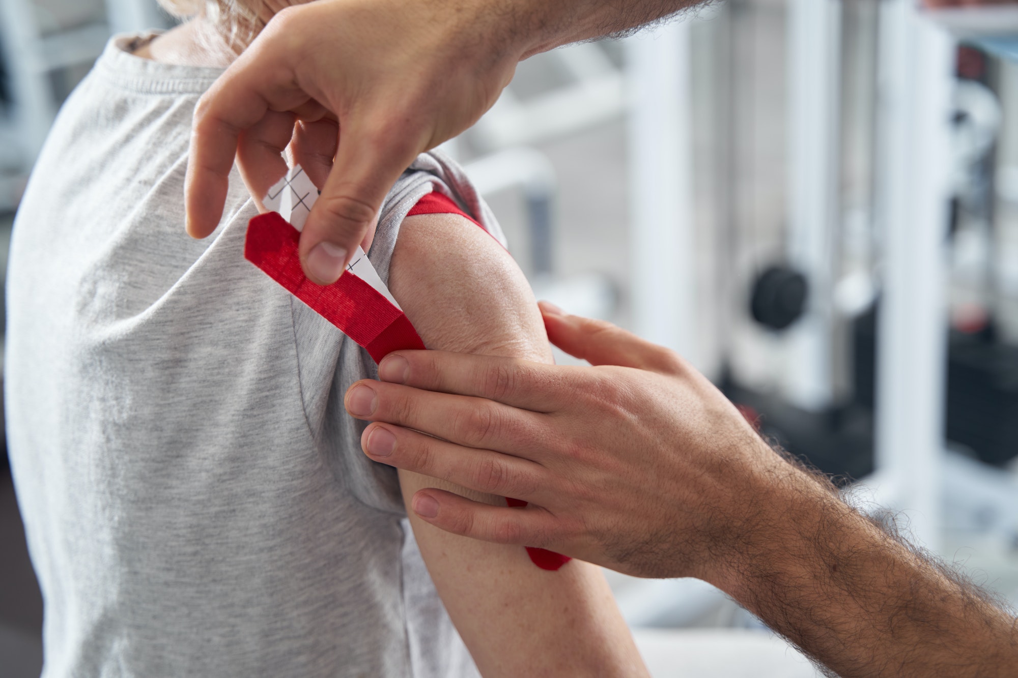Male doctor putting red kinesiology tape on pensioner arm